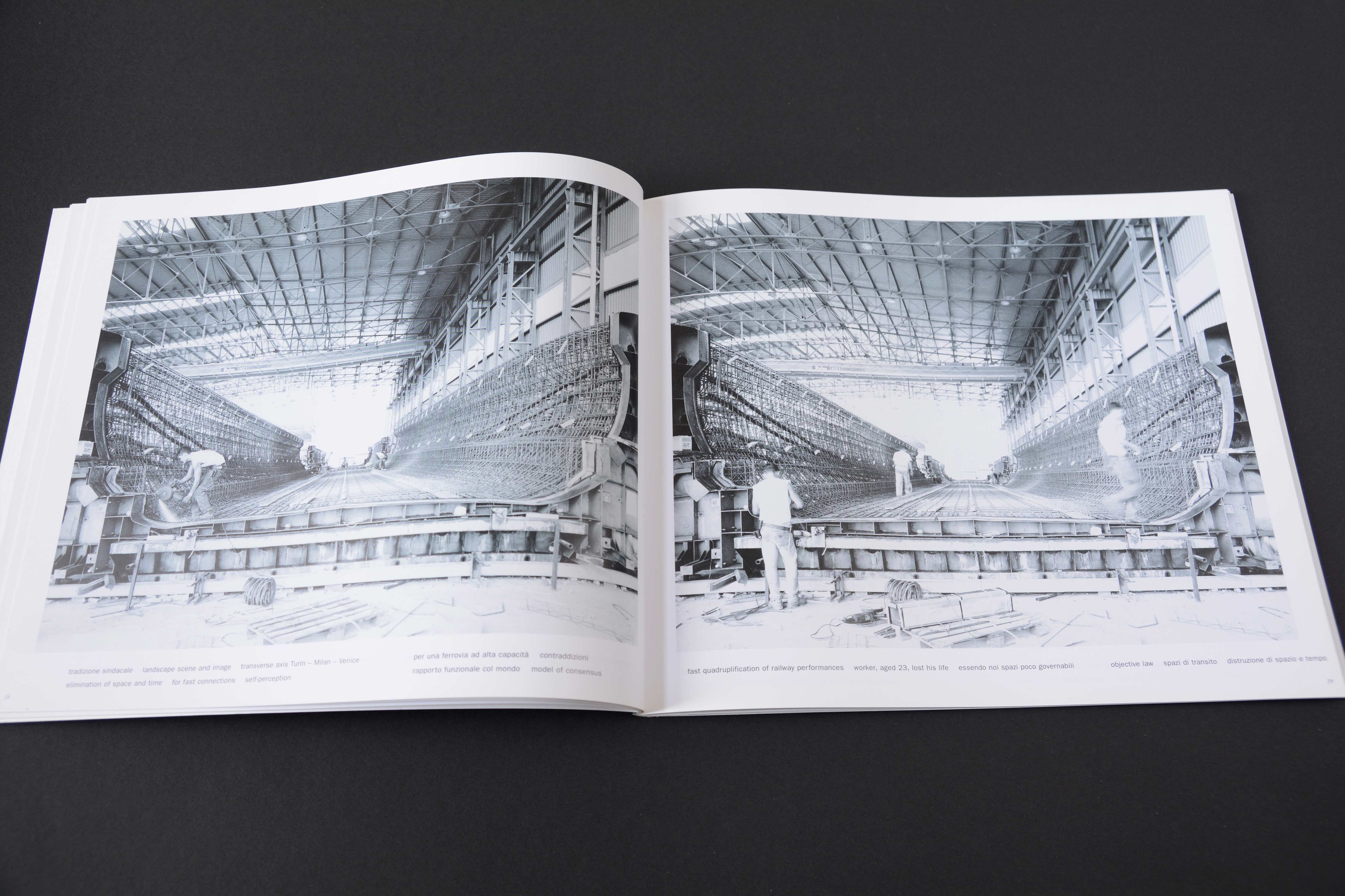 Double page. Large b/w photo with white space around on each page. View into skeleton of bridge in contruction. Workers around. Lines of small text at bottom.