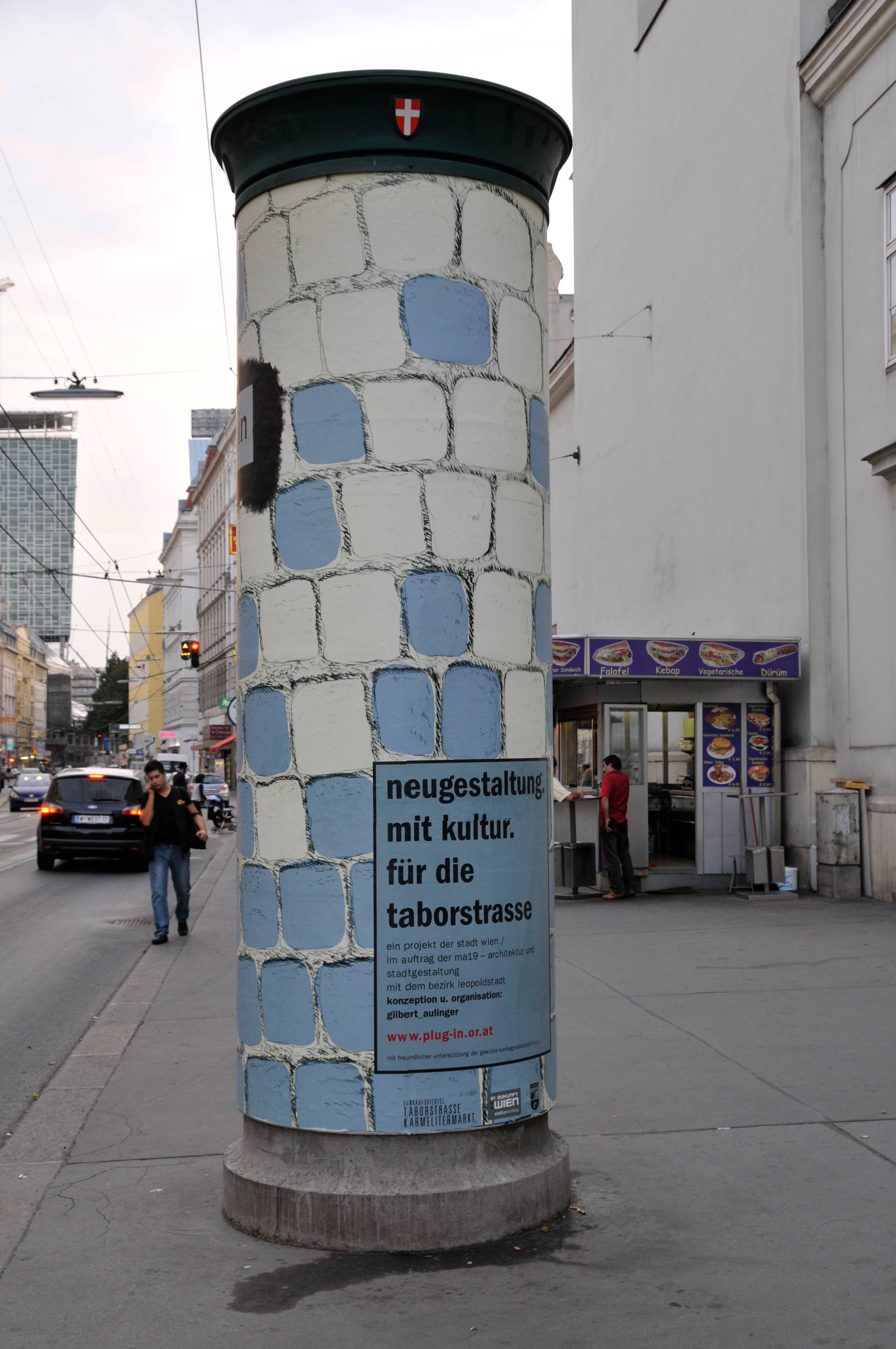 Other side of large advertising pillar. Illustrated cobblestone floor allover. Box with text overlayed.