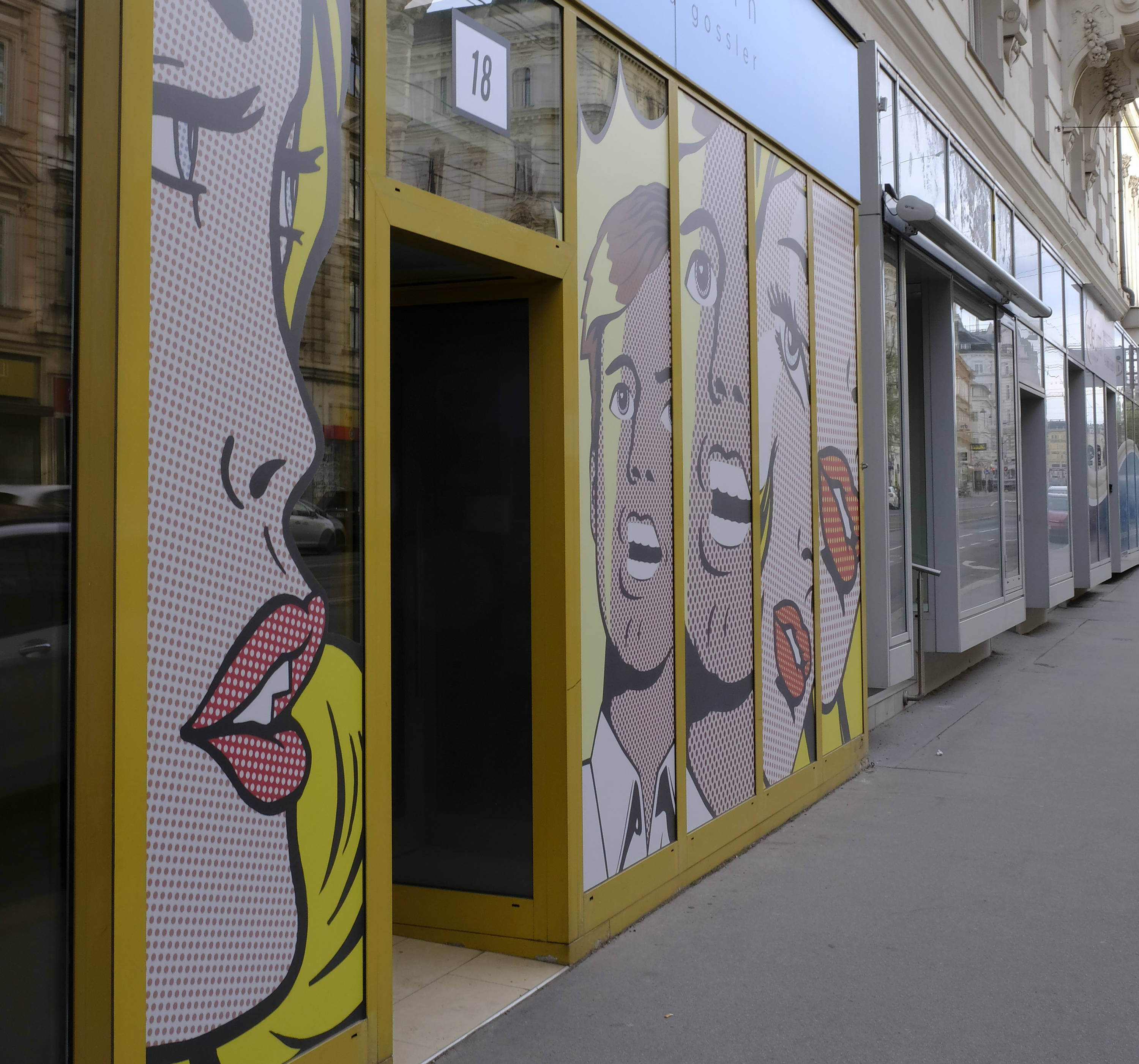 Facade of large glass windows in the street. Full front covered with pop-art style illustrations. Each window contains cropped part of face.