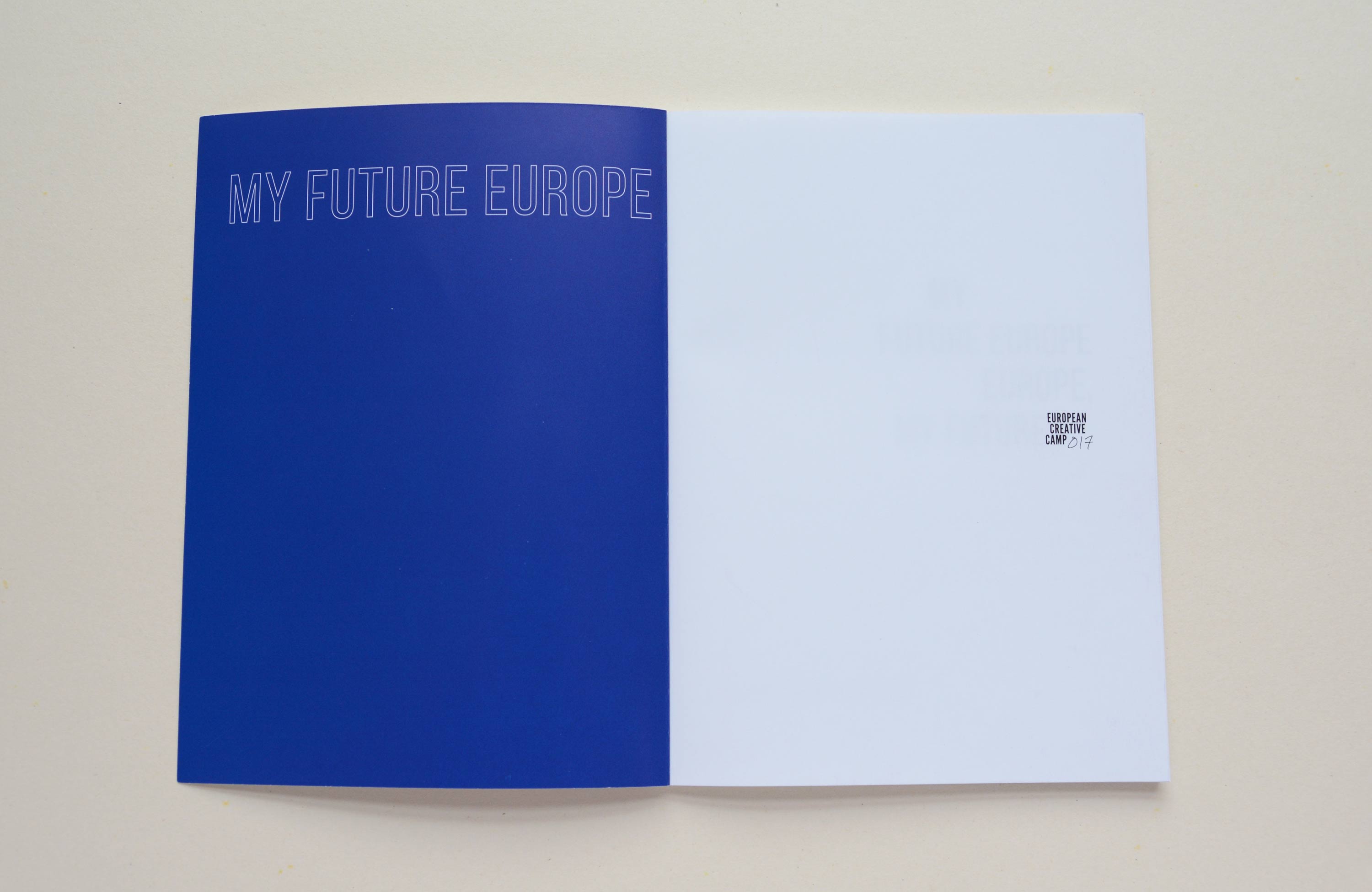Double Page. Left: Blue inside of cover. Large outline font at top. Right: Blank page with small logo.