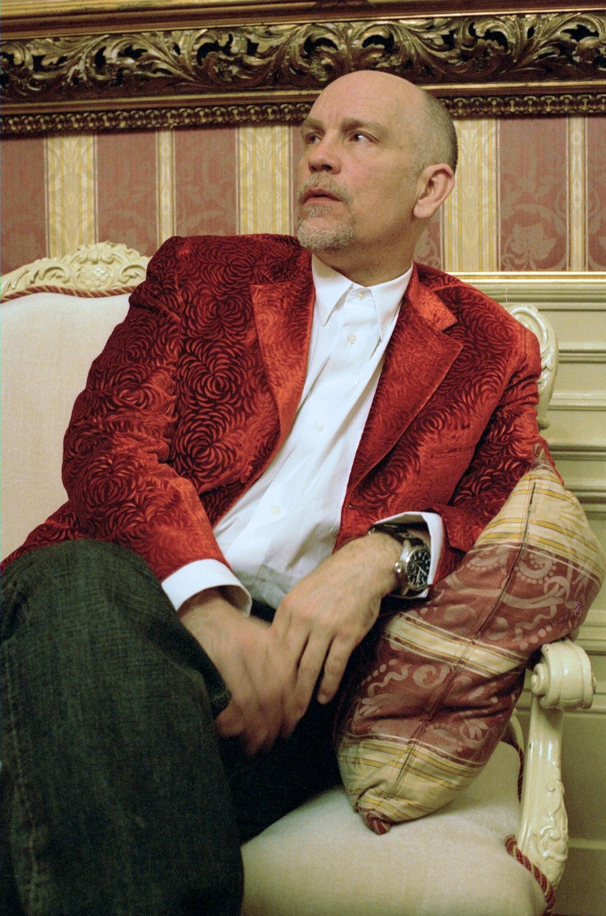 John Malkovic sits on Couch in splendid room.
