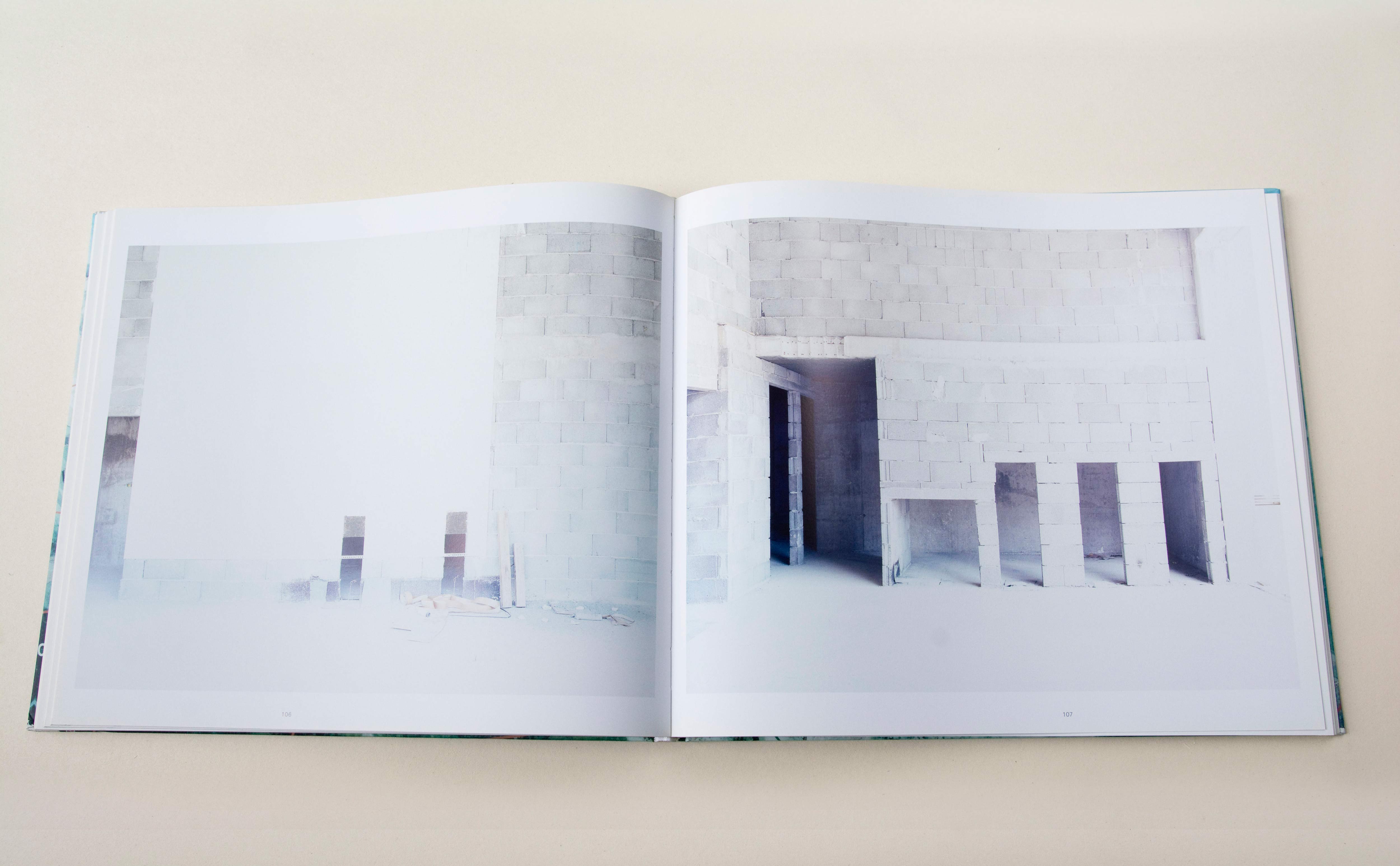Double page. Large photo with white space around on each page. Left: Grey brick wall in construction. Right: Inside a building made of grey bricks.