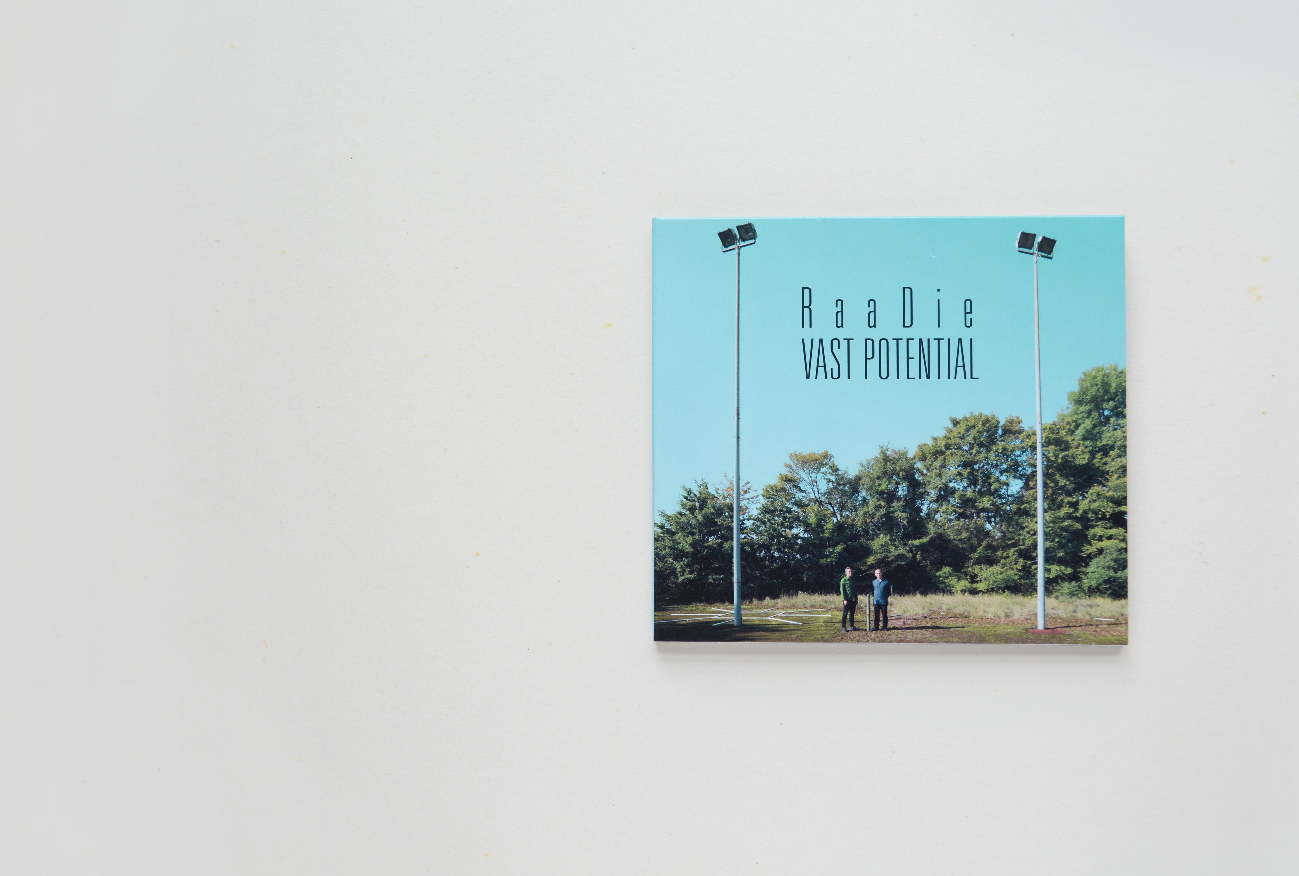 Cover CD. Full-page photo. Distance shot of 2 man standing in between 2 light poles on an abandoned tennis court. Title is set in thin condensed font in upper part.