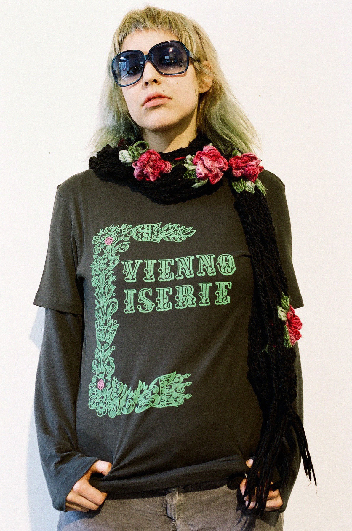 Girl posing with dark grey t-shirt. Logo and decorative Elements in strong green colour printed on it.